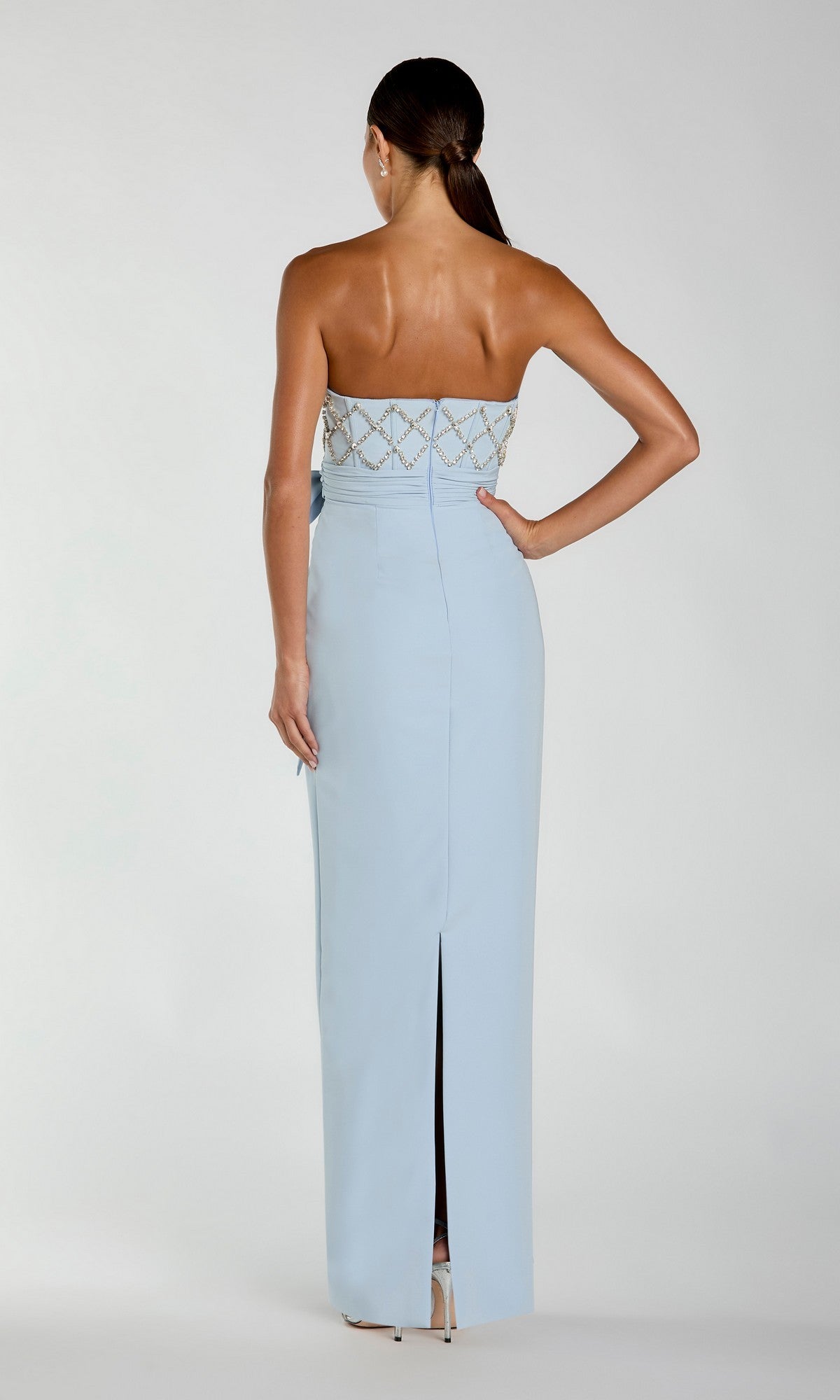A woman faces away from the camera in the Mac Duggal 2294 Strapless Sweetheart Formal Gown—a floor-length, light blue beaded evening dress with a rear slit and intricate beadwork on the bodice.